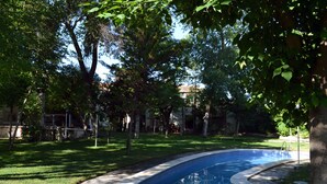A swimming pool surrounded by trees and grass, with a clear sky in the background. - Hostal La Mesnadita (Olmedo)