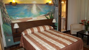 A bedroom with a large bed, two bedside lamps, a nightstand, a chair, a small table with a vase, and a painting of a beach scene on the wall. - Hostal La Mesnadita (Olmedo)