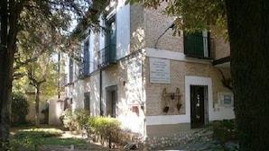 A courtyard with a stone building, a pathway, and greenery. - Hostal La Mesnadita (Olmedo)