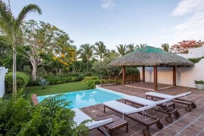 A pool area with lounge chairs, a thatched-roof gazebo, and lush greenery. - Designer Heaven (La Romana)
