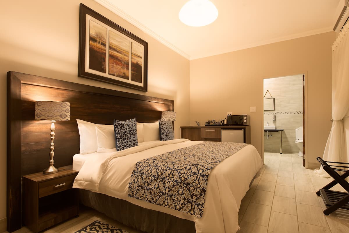 Hotelkamer met een groot bed, nachtkastje met lamp, kast en zichtbare badkamer door een open deur.