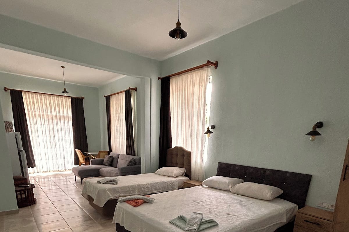 Quarto de hotel com duas camas, um sofá, uma mesa de cabeceira de madeira e um ventilador de teto.