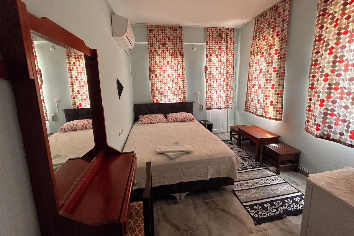 Quarto com cama, escrivaninha, cadeira, espelho e cortinas estampadas.