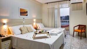 Une chambre d’hôtel avec deux lits, une table de chevet avec un téléphone, un plateau décoré de pétales de rose et une vue sur la ville par la fenêtre.