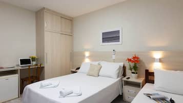 A hotel room with a bed, a desk, a wardrobe, a nightstand, and a small refrigerator.