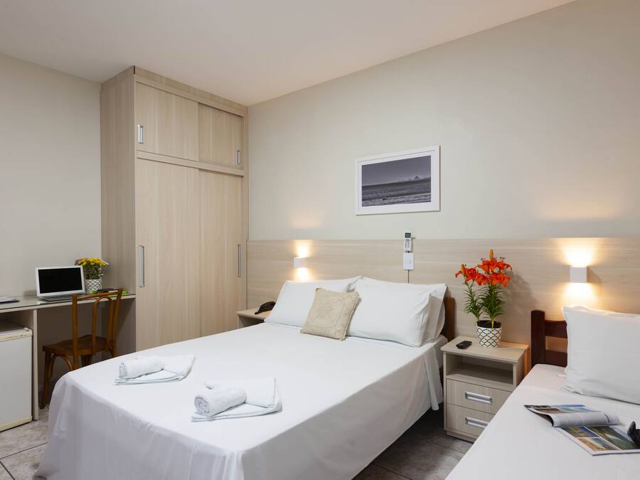 A hotel room with a bed, a desk, a wardrobe, a nightstand, and a small refrigerator.