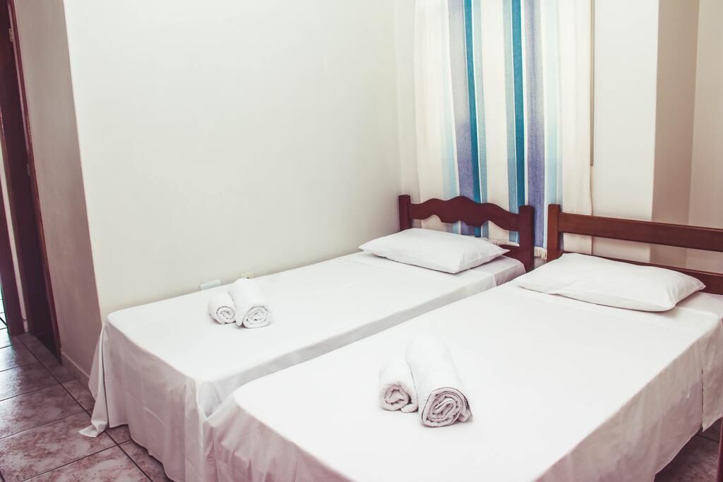 Two single beds with wooden headboards, white linens, and rolled towels.