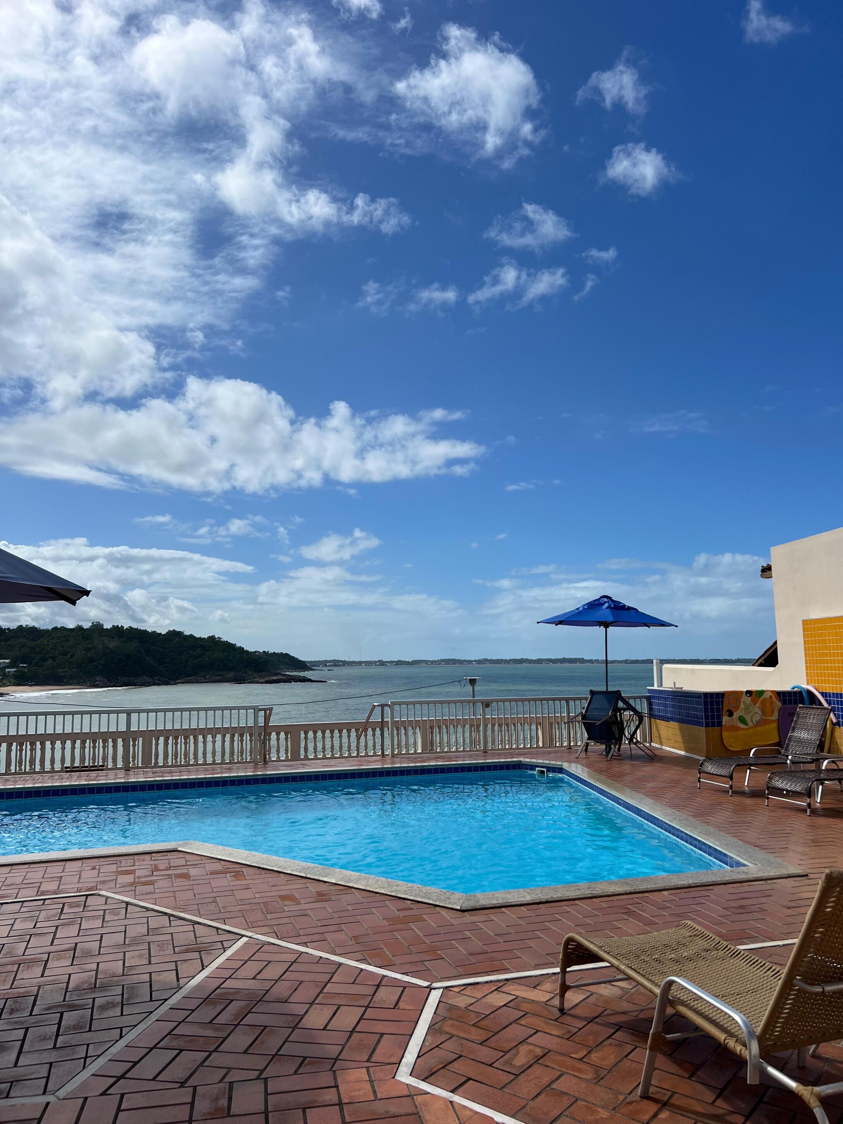 Piscina com vista para o mar, um deck de madeira e algumas cadeiras de descanso.