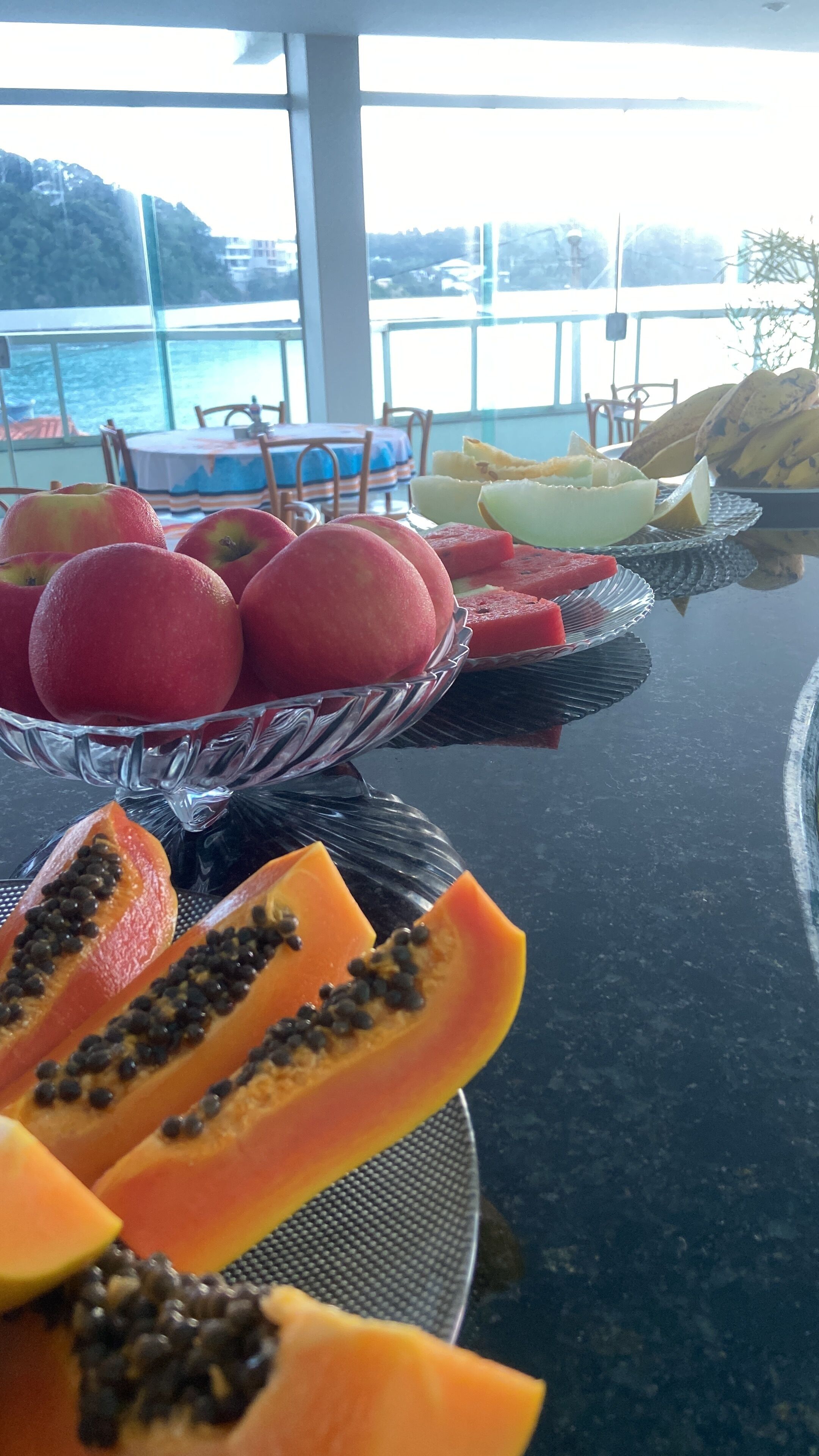 Uma mesa de buffet com diversas frutas, incluindo maçãs, melancia e mamão.
