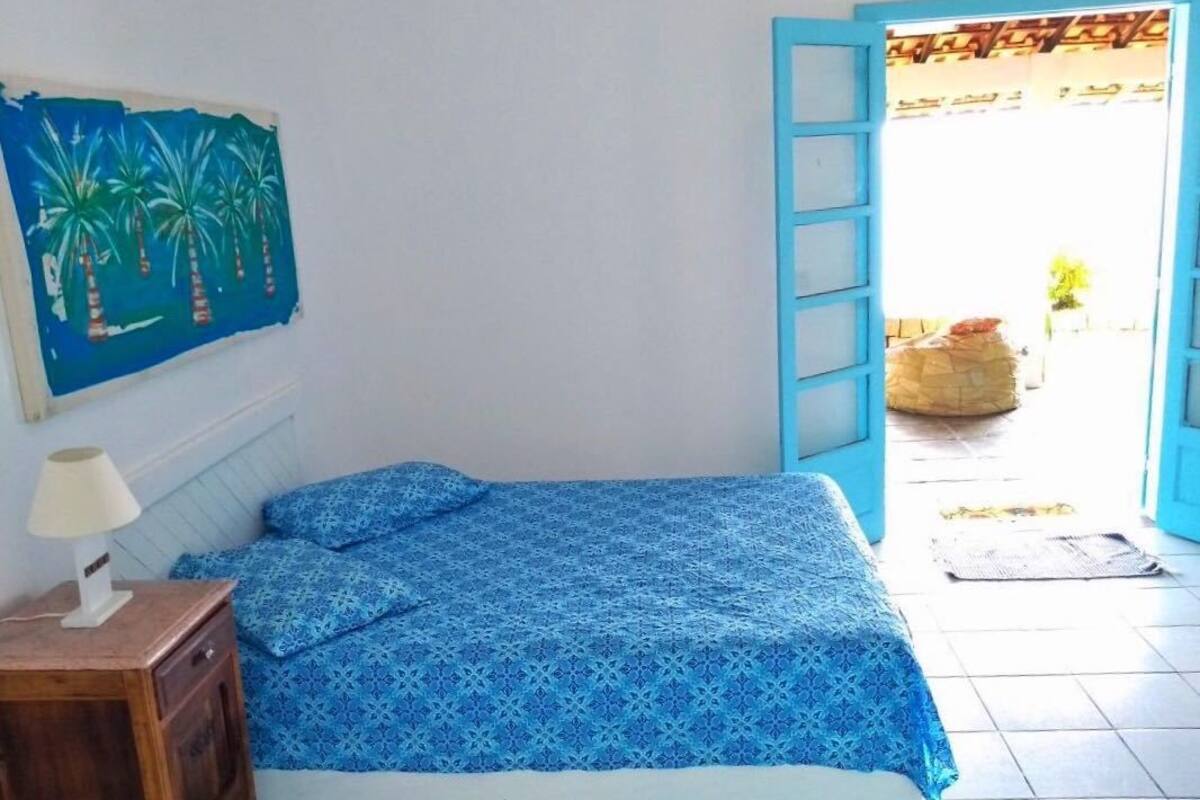 A bedroom with a bed, a nightstand, a painting, and an open door leading outside.