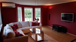 Ein Wohnzimmer mit einem weißen Sofa, roten Kissen, einem Glastisch und einem an der Wand befestigten Flachbildfernseher.