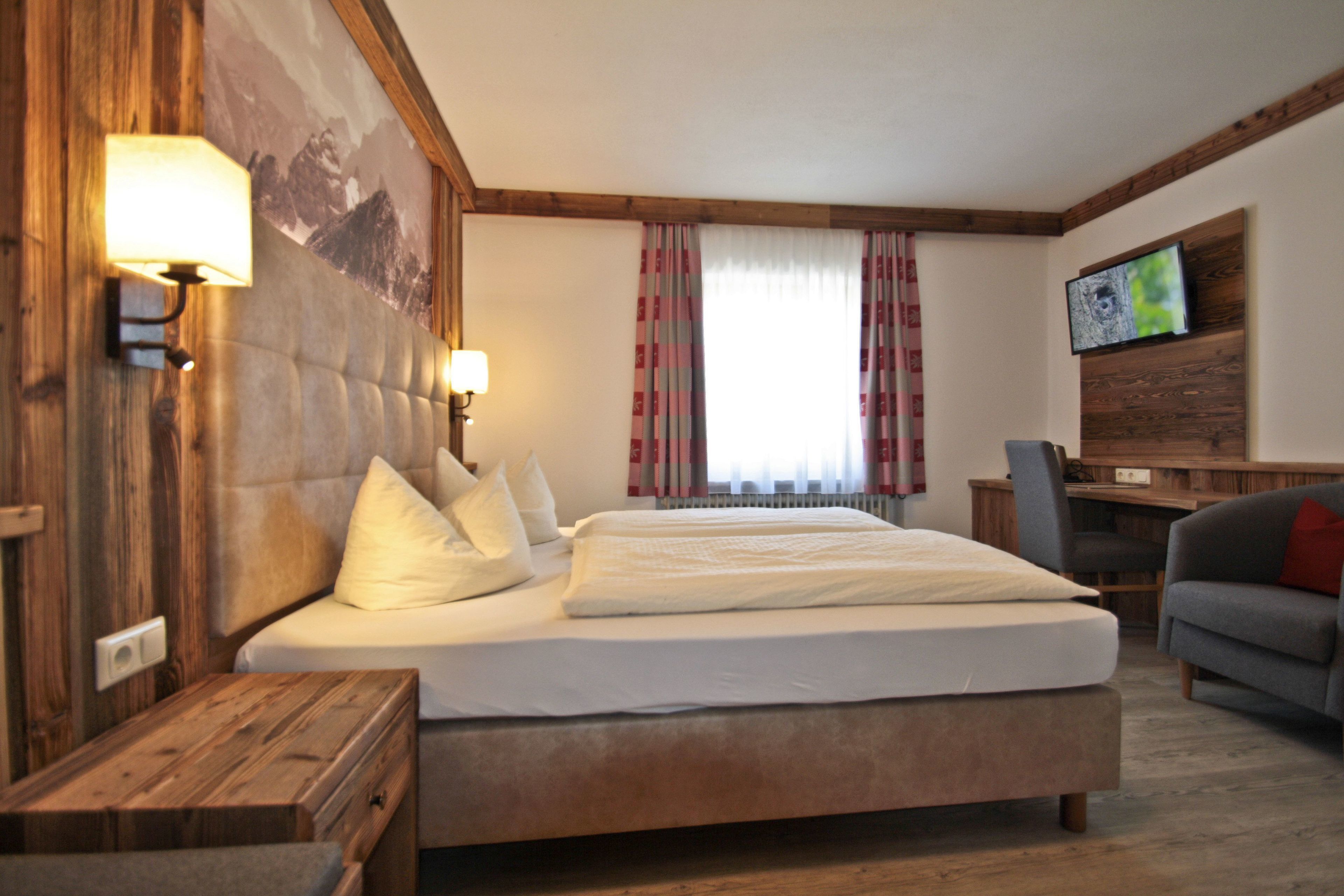 A bedroom with a large bed, wooden headboard, bedside tables, a desk, and a television.