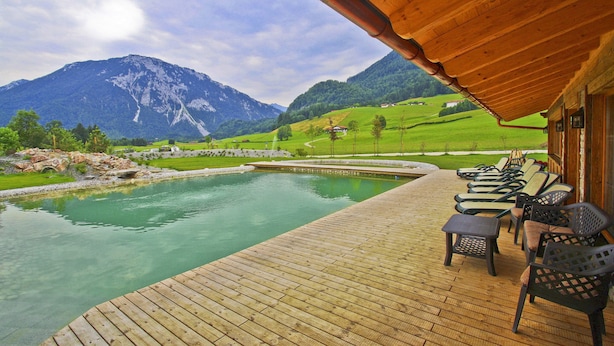 A wooden deck with outdoor seating, a pool, and a mountain backdrop. - Zeller Hof (Ruhpolding)