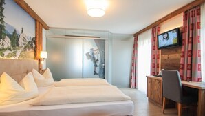 A hotel room with a large bed, a desk with a chair, a television, and a view of a mountain landscape. - Zeller Hof (Ruhpolding)
