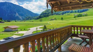 A wooden balcony with a view of a green valley, a winding road, and distant mountains. - Zeller Hof (Ruhpolding)