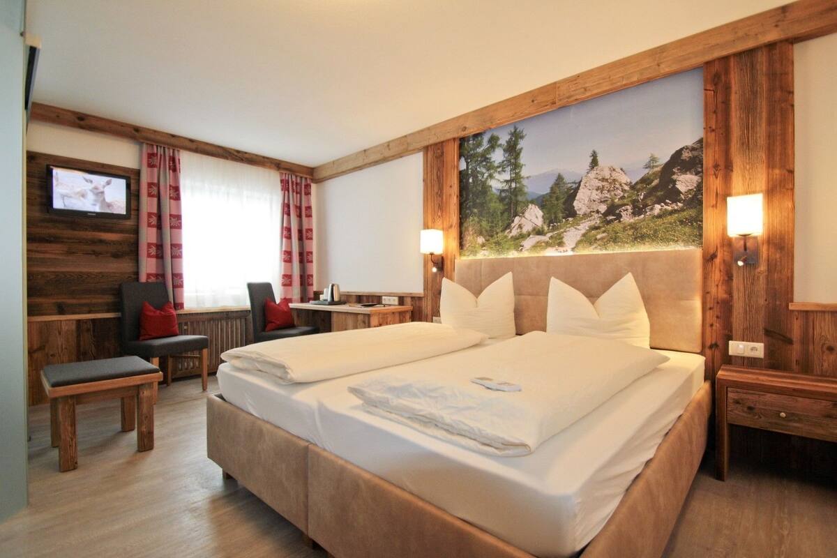 Ein Hotelzimmer mit einem großen Bett, einem Schreibtisch, einem Sessel und einem Fernseher.