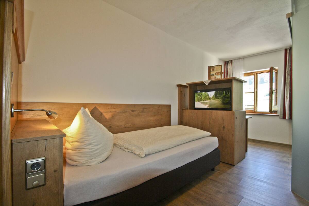 Ein Schlafzimmer mit einem Holz-Kopfteil, einem Nachttisch mit Lampe, einem Bett mit Kissen und einer kleinen Holzkabine.