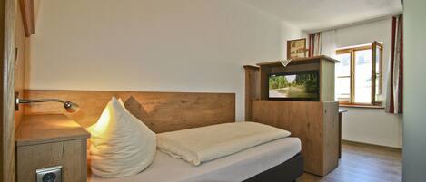 A bedroom with a wooden headboard, a bedside table with a lamp, a bed with pillows, and a small wooden cabinet.