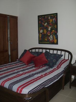 A bedroom with a bed, pillows, a wooden door, and a colorful painting on the wall. - Juan Dolio Apartment (Guayacanes)