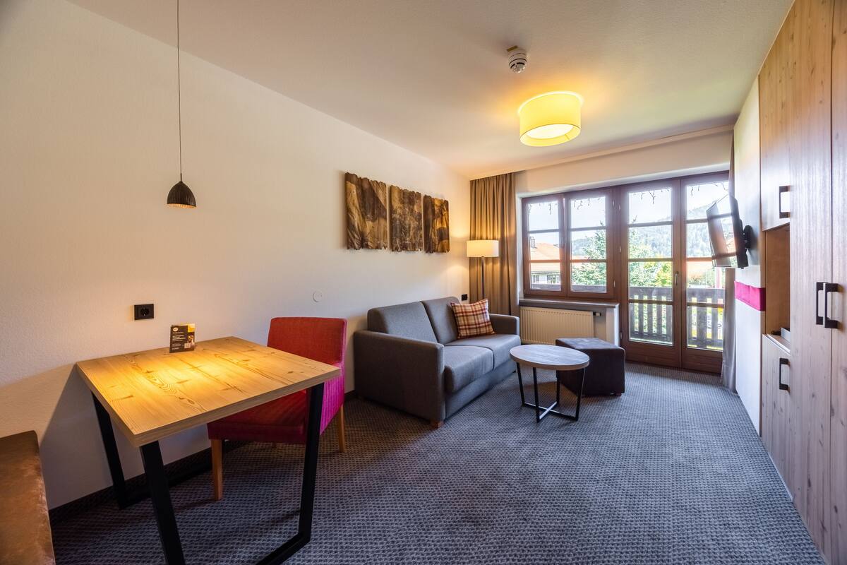 A modern room with a wooden table, a sofa, a small round table, and a large window with a view.
