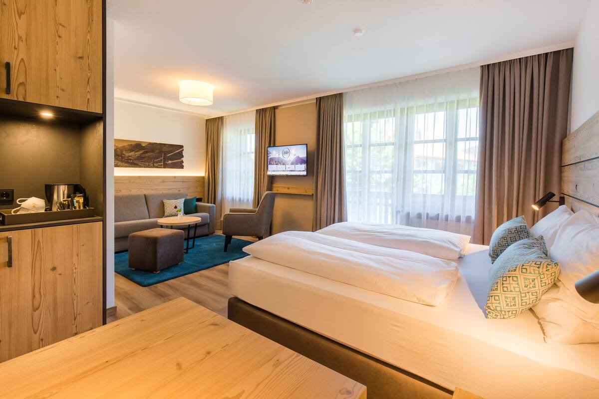 A hotel room with a wooden cabinet, a sofa, a TV mounted on the wall, and a bed with patterned pillows.
