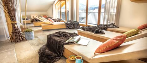 Una habitación acogedora con techo inclinado, ventanas amplias y vistas a las montañas. Hay dos camas con almohadas y una mesita con una taza y un tazón.