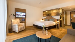 Una habitación de hotel moderna con una cama, un televisor, una silla, una mesita y un espejo.
