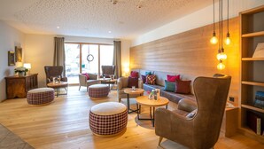 Una sala de estar moderna con suelo de madera, un sofá, sillones, otomanas y una estantería.