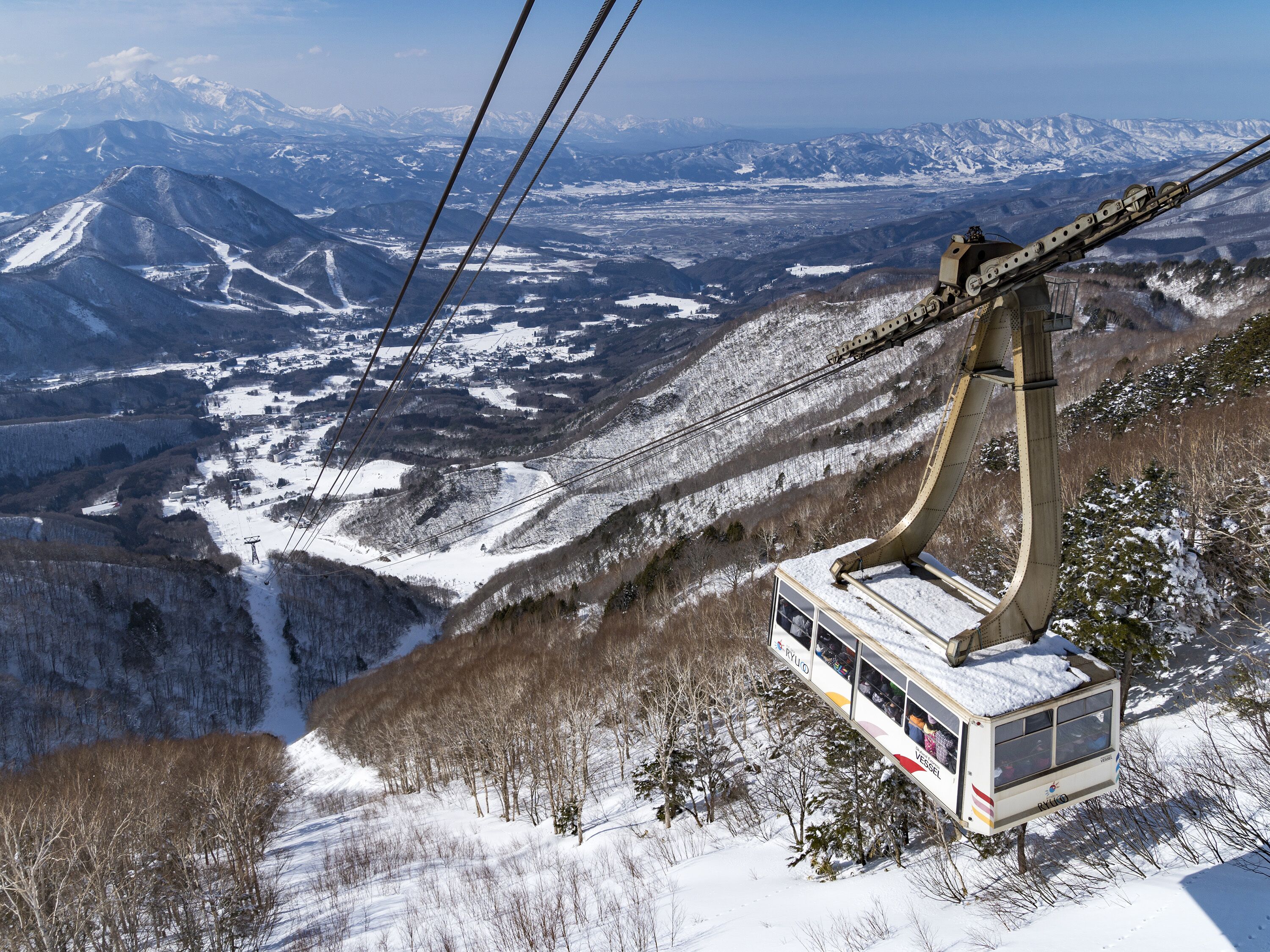 A cable car system with a cabin suspended by cables, offering a view of a snowy mountainous landscape.