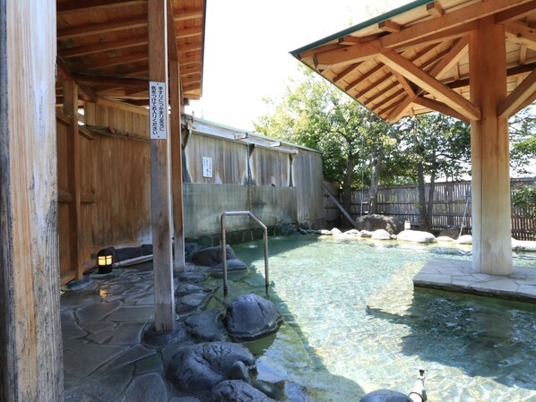 A traditional wooden bathhouse with a stone-paved area and a clear water pool.