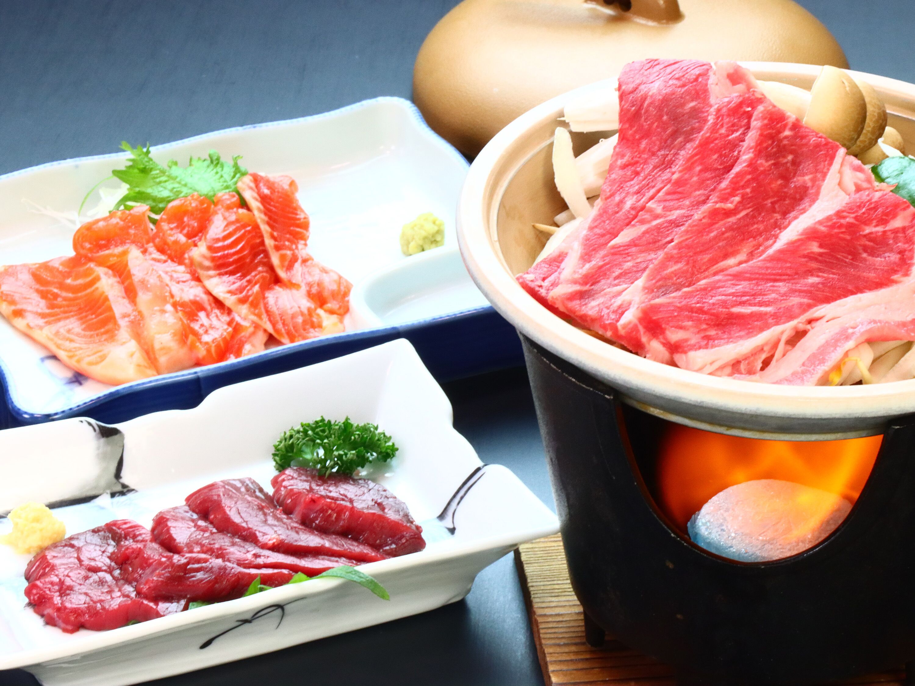 A hot pot with raw meat and vegetables, and two plates with sliced meat and vegetables.