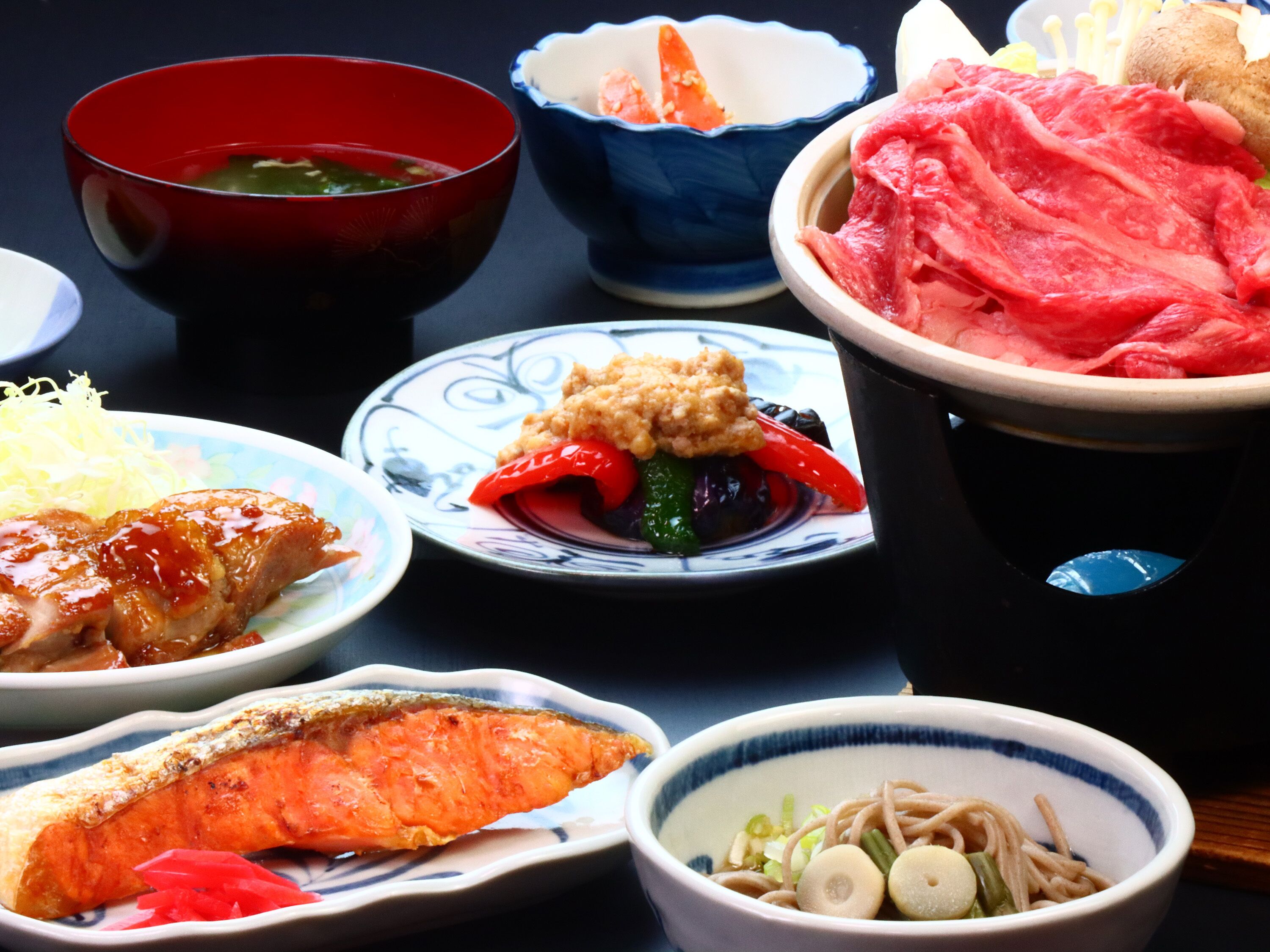 A variety of dishes including salmon, beef, and vegetables, served in traditional bowls.