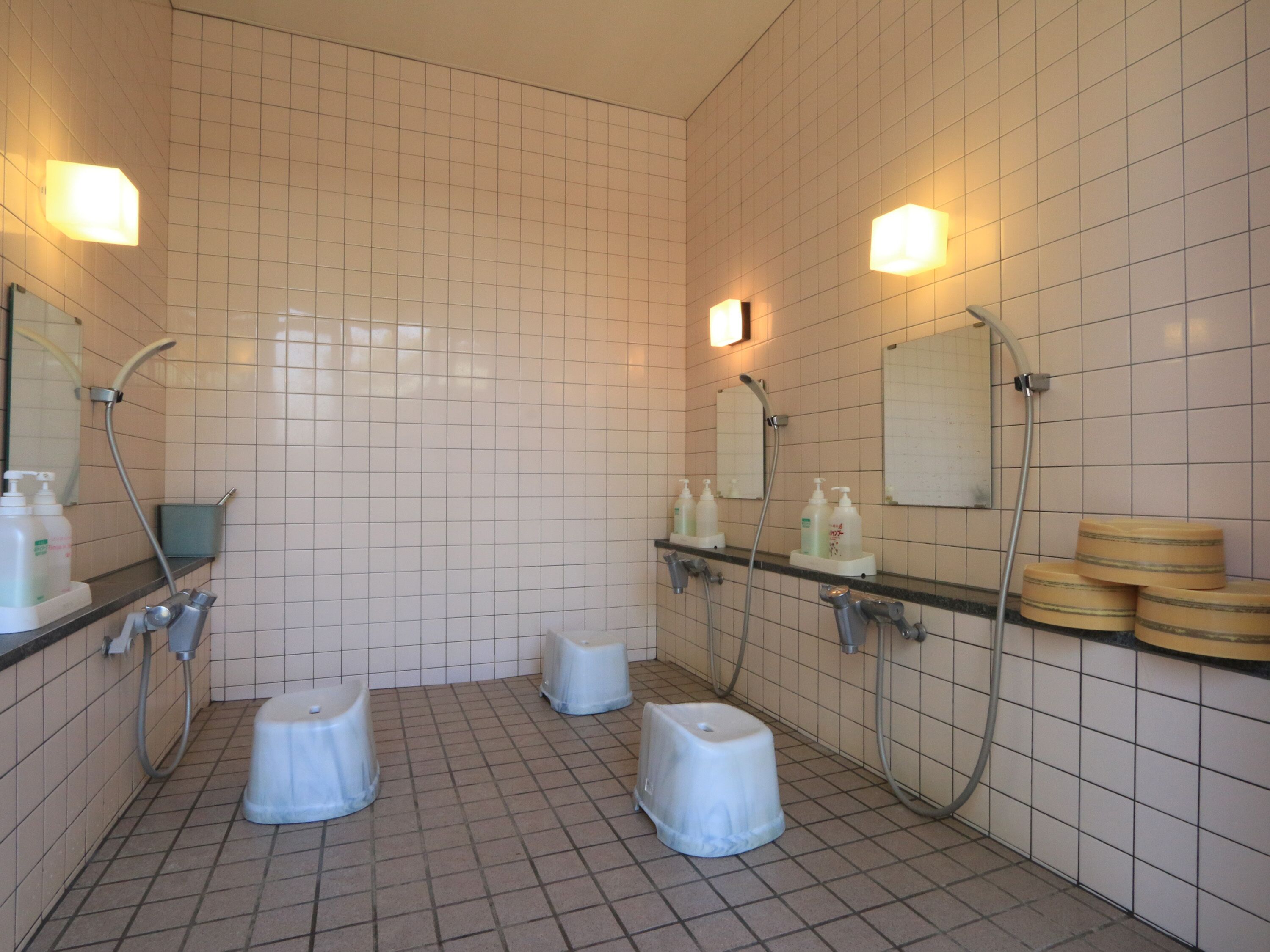 A public restroom with tiled walls, a mirror, a sink, and two toilet stalls.