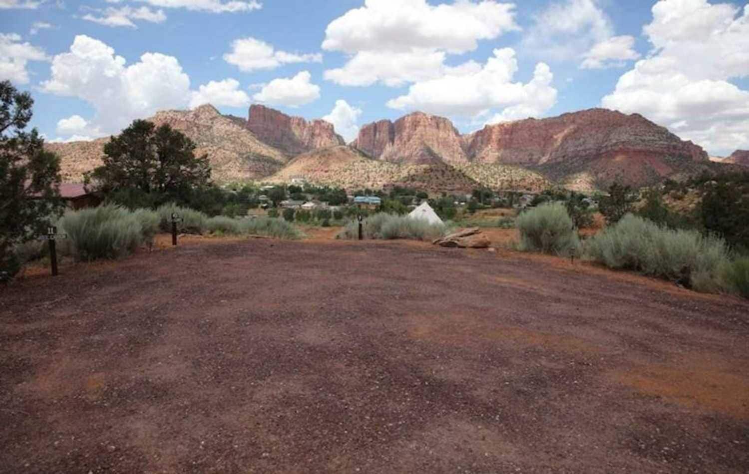 A large open area with a dirt ground, surrounded by sparse vegetation and a mountainous backdrop.