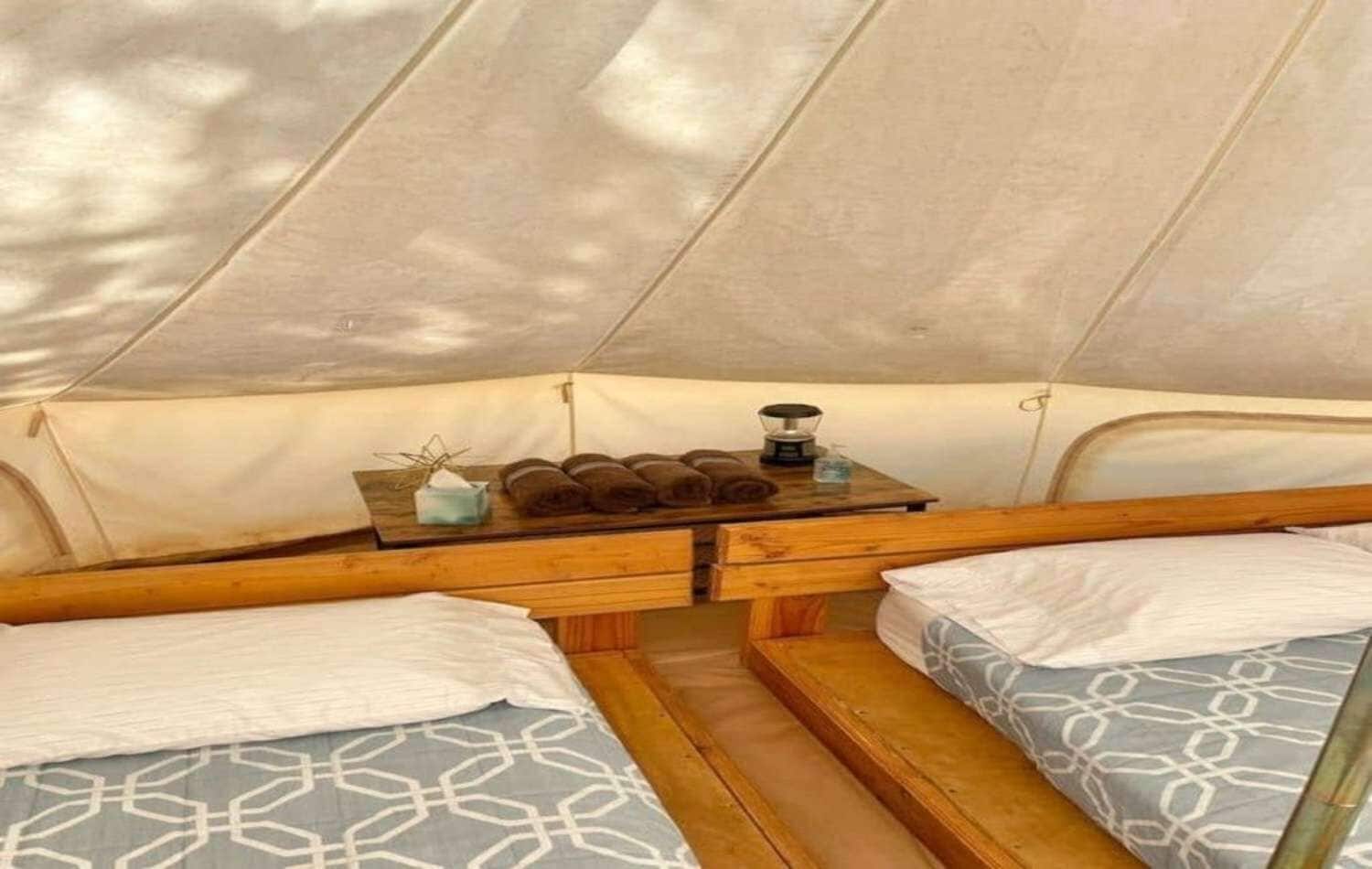 A tent interior with two beds, a table with towels and a kettle, and a window.