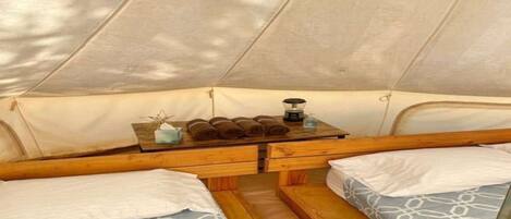 A tent interior with two beds, a table with towels and a kettle, and a window.