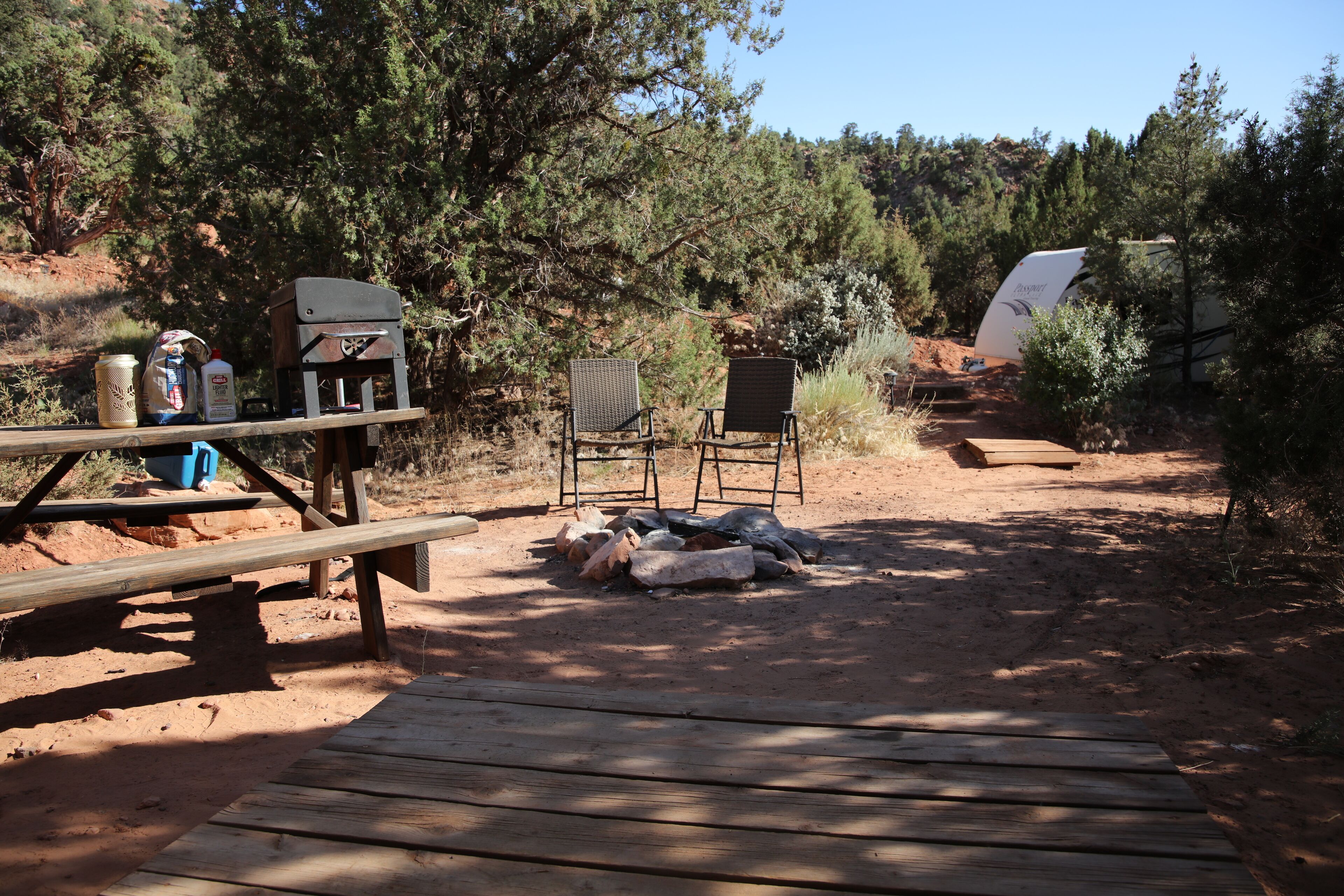 Un camping con mesa de picnic, dos sillas, una parrilla y una tienda de campaña.