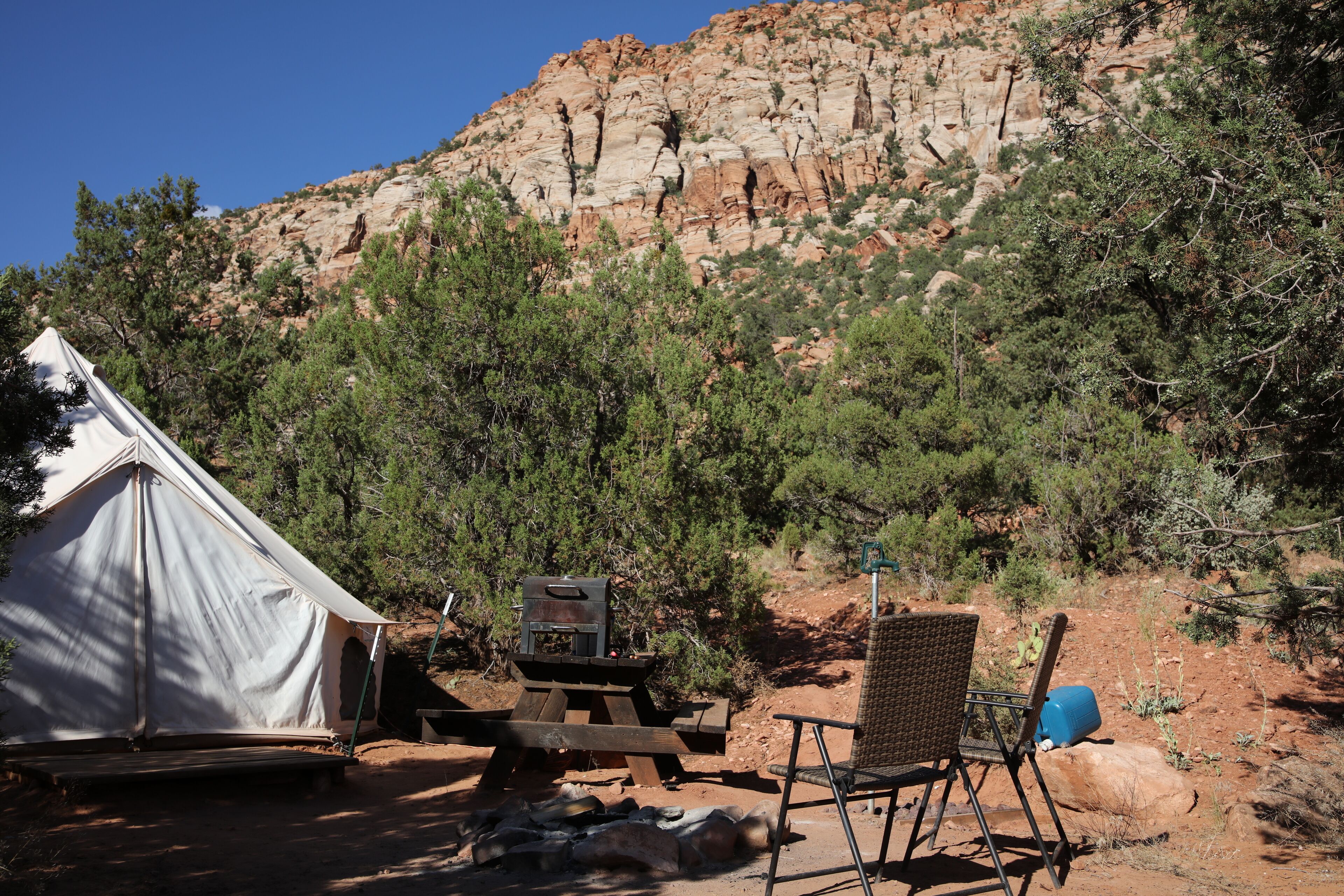 A tent, a grill, and a chair in a campsite with a rocky mountain in the background.