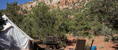 A tent, a grill, and a chair in a campsite with a rocky mountain in the background.
