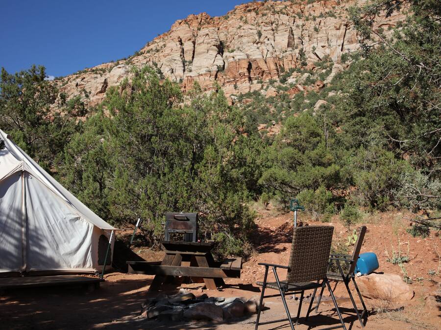 A tent, a grill, and a chair in a campsite with a rocky mountain in the background.