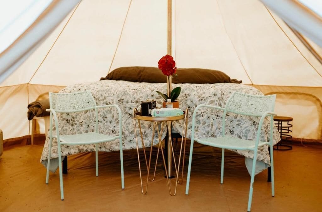 A tent with a bed, two chairs, a table, and a rose.