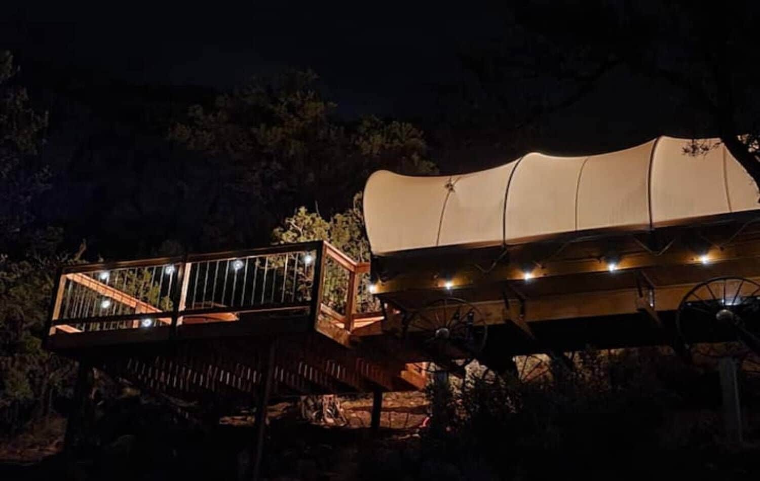 A tented structure with a wooden deck and a glass railing, surrounded by trees.