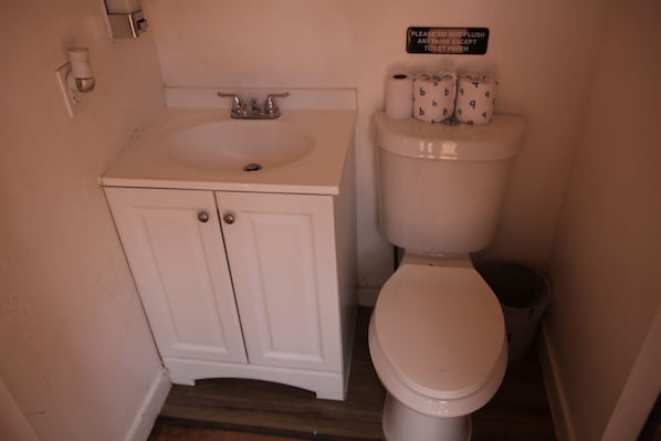 A bathroom with a white sink, cabinet, toilet, and a sign above the toilet.