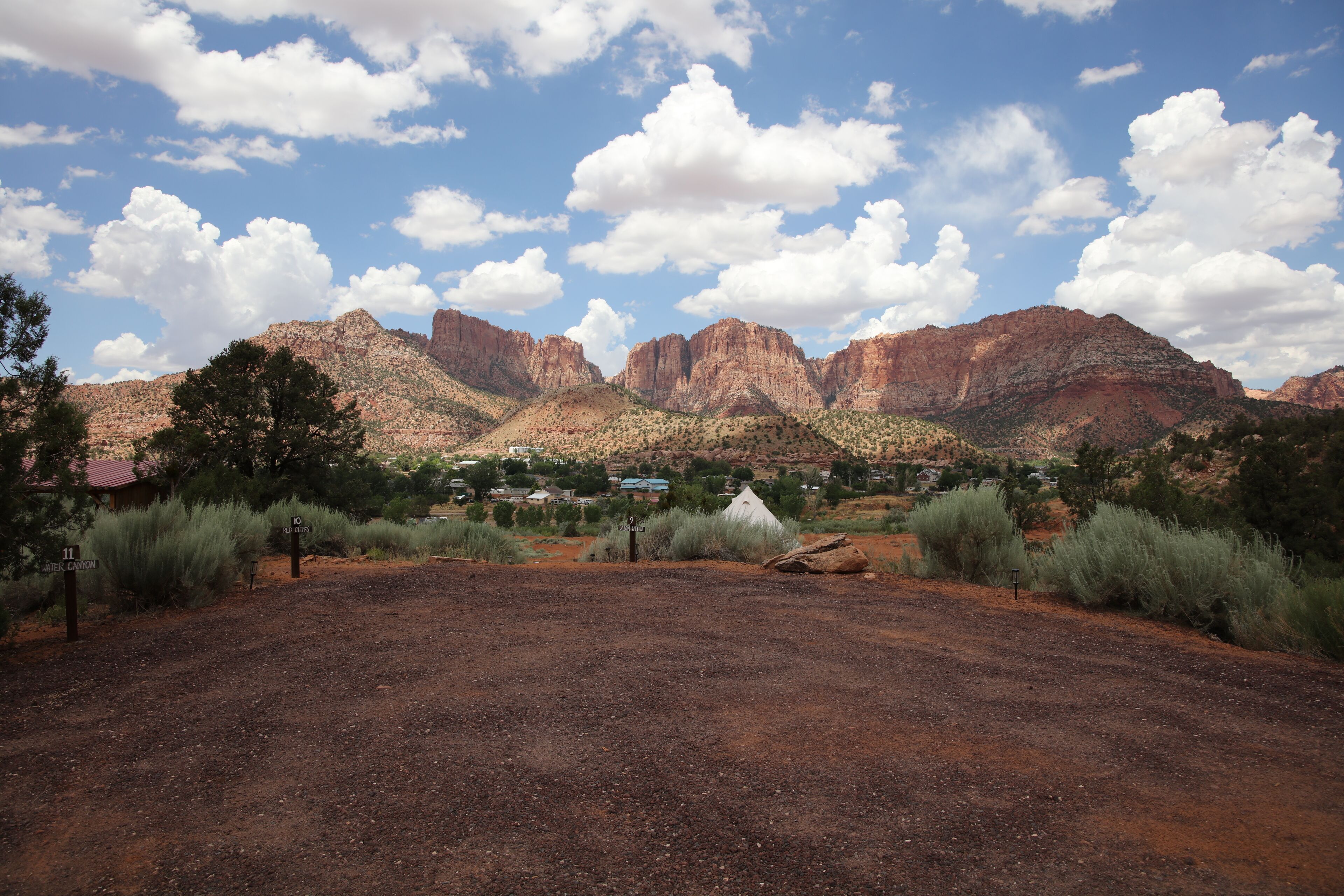 Un paysage désertique caractérisé par des formations rocheuses rouges, une végétation clairsemée et un petit village visible au loin.