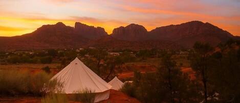 A desert landscape with two white tents and a mountain range in the background.