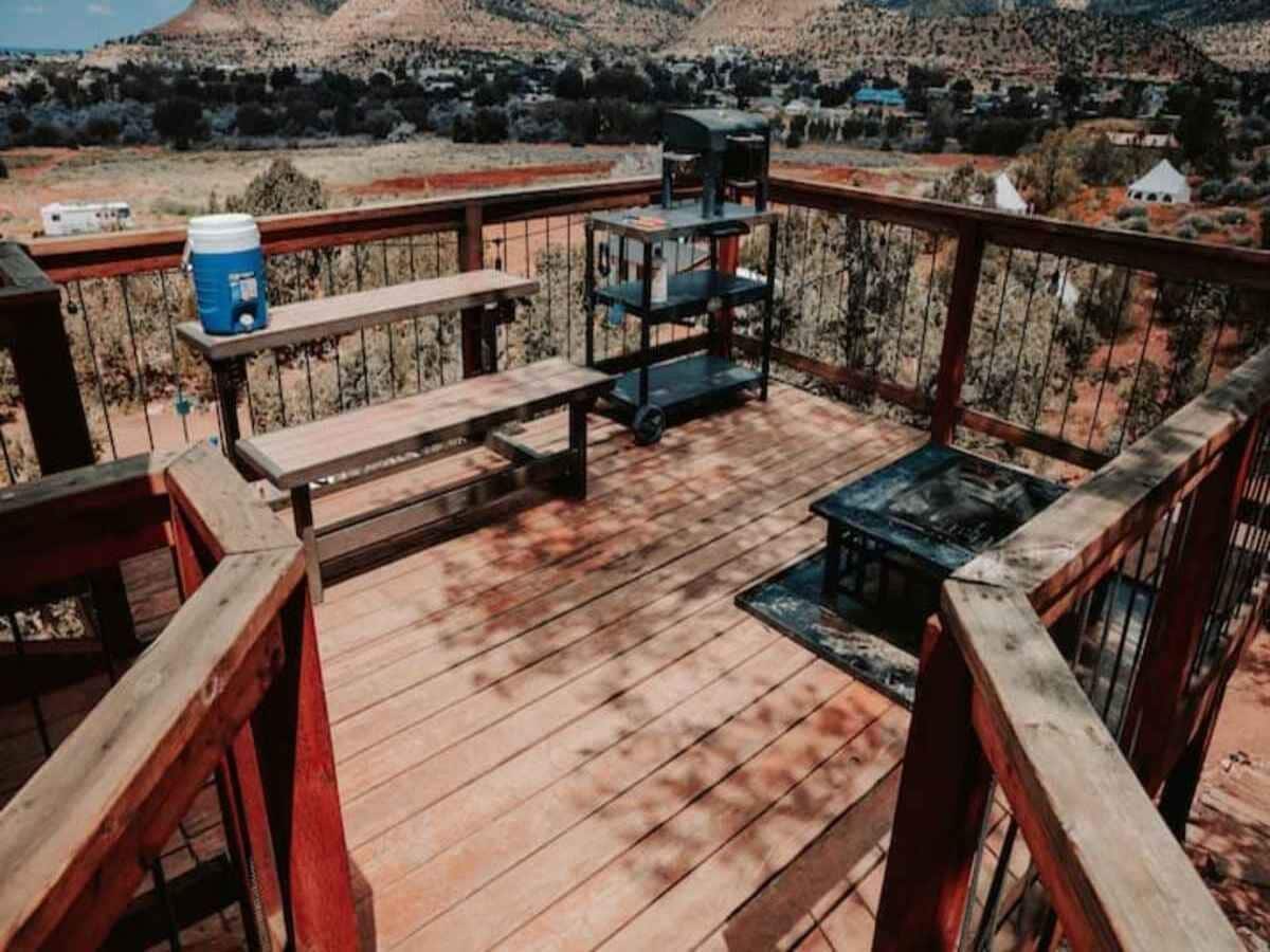 A wooden deck with a metal railing, a blue barrel, a metal table, and a metal shelf unit.