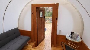 Una habitación acogedora con sofá, una silla, una puerta de madera que da al exterior y una alfombra de cuero de vaca.
