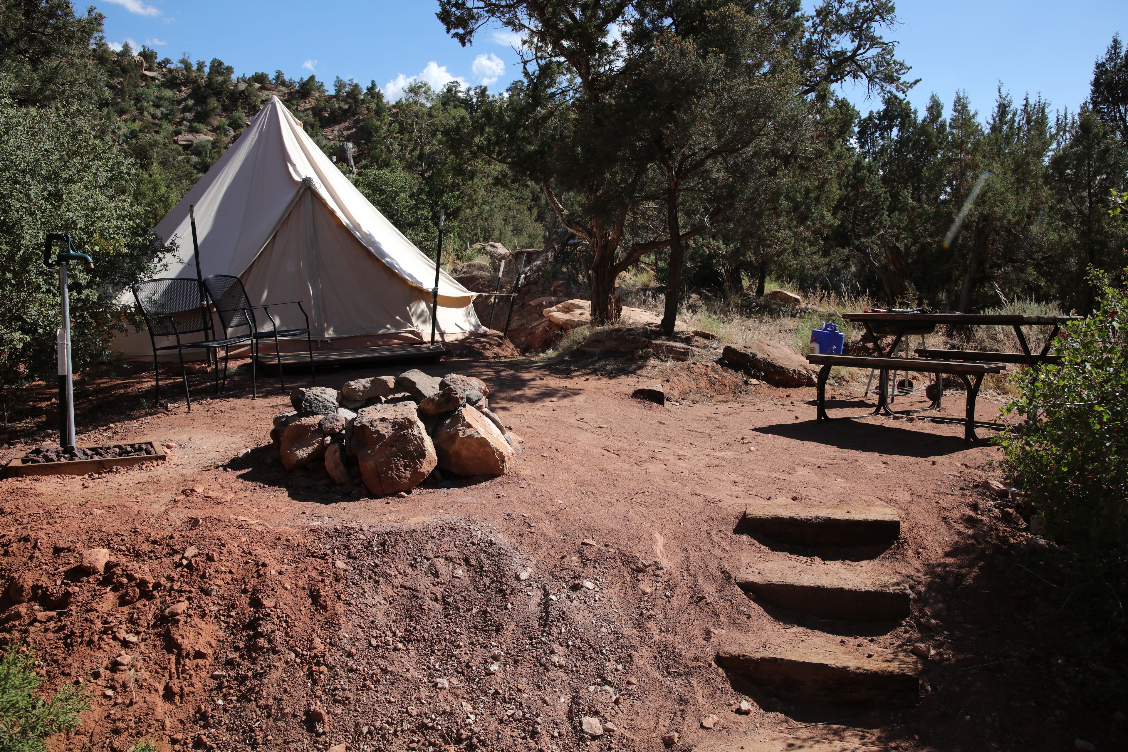 A tent with a picnic table nearby, surrounded by rocks and trees.