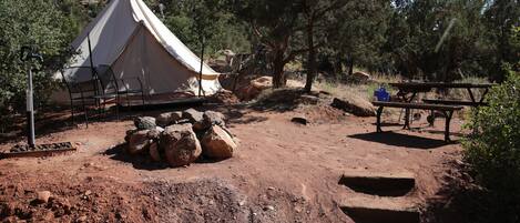 A tent with a picnic table nearby, surrounded by rocks and trees.