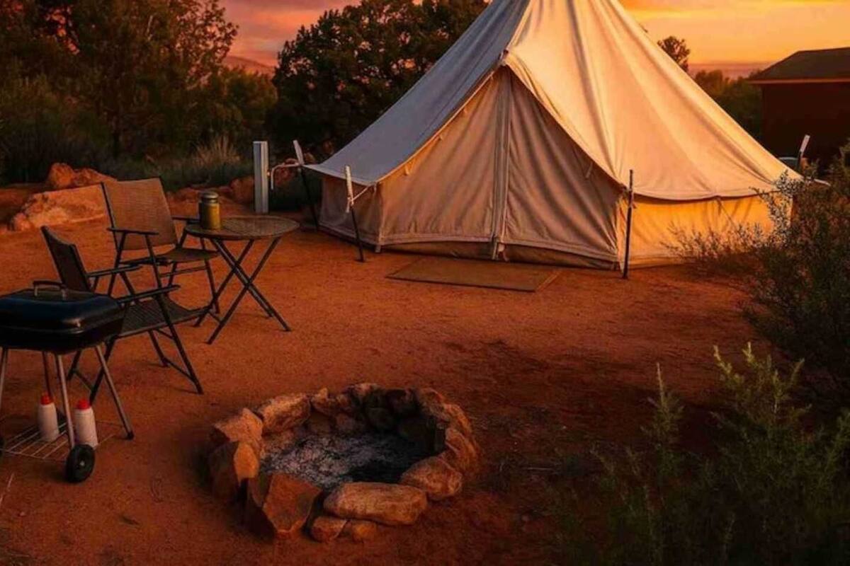 A tent set up in a natural environment with a fire pit and camping chairs.